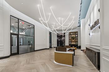 A modern interior with a long hallway, a reception desk, and a large chandelier.